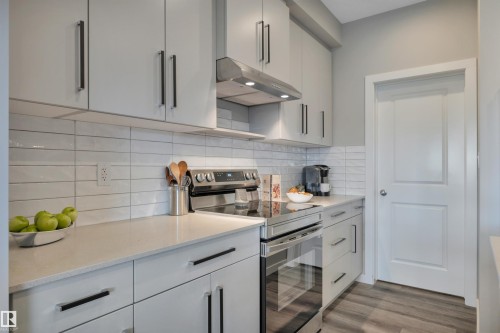 Kitchen featuring light gray cabinetry with black hardware, white subway tile backsplash, stainless steel appliances, and light-toned countertops - 157 Larch Crescent, Leduc, AB 
