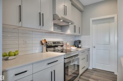 Kitchen featuring light gray cabinetry with black hardware, white subway tile backsplash, stainless steel appliances, and light-toned countertops - 