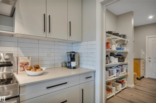 Contemporary kitchen featuring light-toned cabinetry with black hardware, a white subway tile backsplash, and a light countertop - 157 Larch Crescent, Leduc, AB 