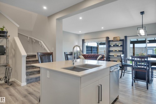 Open-concept kitchen featuring a center island with an undermount double-basin sink, stainless steel dishwasher, and light-toned countertops - 157 Larch Crescent, Leduc, AB 