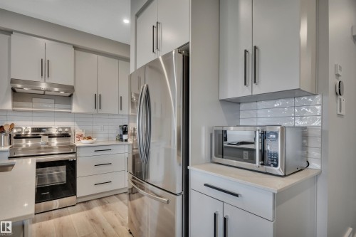 Kitchen featuring light-toned cabinetry with dark hardware, stainless steel appliances, and wood-finish flooring - 157 Larch Crescent, Leduc, AB 