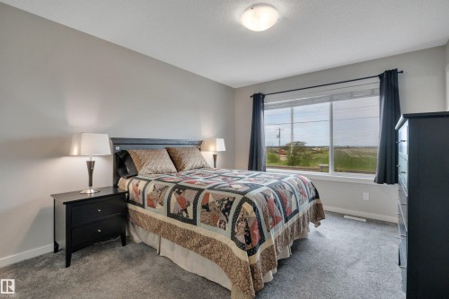 Carpeted bedroom with a large window and neutral wall tones - 157 Larch Crescent, Leduc, AB 