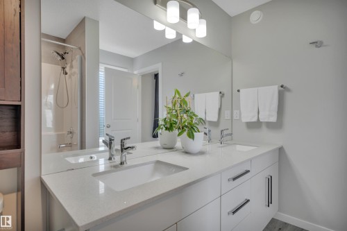Double vanity featuring white cabinetry, integrated sinks, chrome hardware, and a full-width mirror - 157 Larch Crescent, Leduc, AB 