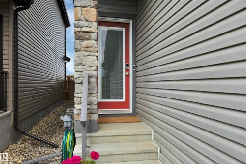 Front entry featuring a red framed door with glass insert, stone pillar accent, and concrete steps - 157 Larch Crescent, Leduc, AB 