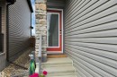 Front entry featuring a red framed door with glass insert, stone pillar accent, and concrete steps - 157 Larch Crescent, Leduc, AB 