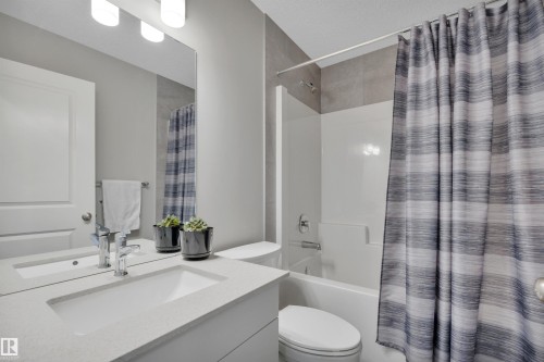 Bathroom featuring a white bathtub with a tiled shower surround, a vanity with an integrated sink, a large wall-mounted mirror, and an overhead light fixture - 157 Larch Crescent, Leduc, AB 