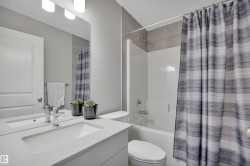 Bathroom featuring a white bathtub with a tiled shower surround, a vanity with an integrated sink, a large wall-mounted mirror, and an overhead light fixture - 