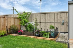Manicured lawn with a landscaped garden bed, featuring a wood fence, mature greenery, and decorative wrought iron fencing - 