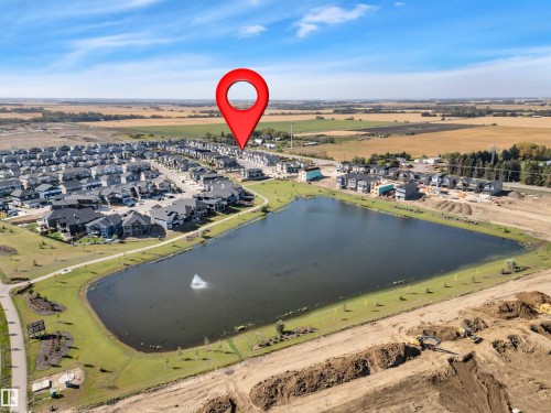 Aerial perspective highlighting a developed residential area bordering a serene pond with an active fountain - 157 Larch Crescent, Leduc, AB 