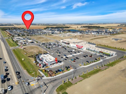 Aerial perspective highlighting a commercial development with a substantial parking lot, multiple retail buildings, and surrounding residential areas - 157 Larch Crescent, Leduc, AB 