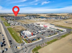 Aerial perspective highlighting a commercial development with a substantial parking lot, multiple retail buildings, and surrounding residential areas - 