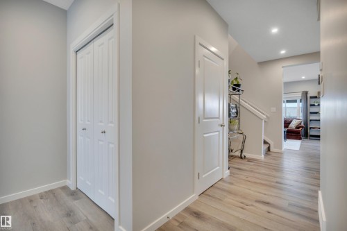 Hallway featuring wood-finish flooring, light grey painted walls, white baseboards, and bright recessed lighting - 157 Larch Crescent, Leduc, AB 