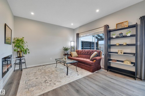 Spacious living area featuring light gray walls, recessed lighting, wood-finish flooring, a contemporary linear fireplace, and a large window - 157 Larch Crescent, Leduc, AB 