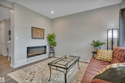 Living area featuring an integrated linear electric fireplace, recessed ceiling lighting, and wood-finish flooring - 157 Larch Crescent, Leduc, AB 