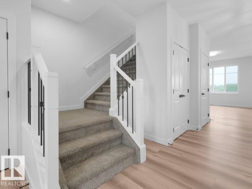 Carpeted staircase featuring white newel posts and black iron balusters - 18719 130 Street, Edmonton, AB 