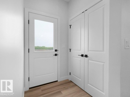 Entryway featuring a white door with transom-style glass, matte black hardware, and wood-finish flooring - 18719 130 Street, Edmonton, AB 