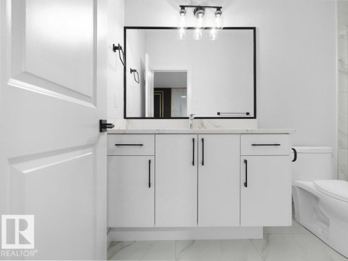 Contemporary bathroom vanity featuring white cabinetry, a light-toned countertop, and a large framed mirror - 18719 130 Street, Edmonton, AB 