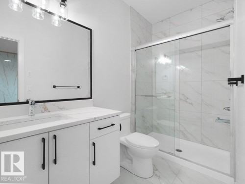 Bathroom featuring a glass-enclosed shower with white tiled walls and floor, a white vanity with a rectangular sink and stone countertop, a large framed mirror, and modern black hardware - 18719 130 Street, Edmonton, AB 