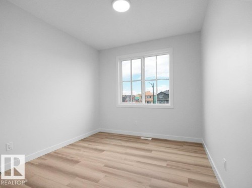 Bright interior space featuring a multi-pane window, wood-finish flooring, white baseboards, and a flush-mount ceiling light - 18719 130 Street, Edmonton, AB 