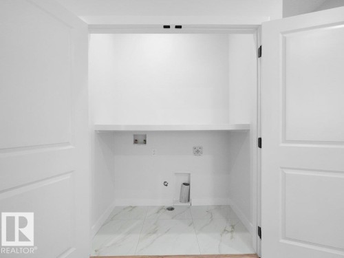 Dedicated laundry closet featuring white paneled double doors, interior shelving, and marble-look tile flooring - 18719 130 Street, Edmonton, AB 