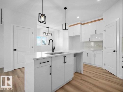Modern kitchen featuring a central island with an undermount sink and matte black faucet, surrounded by white gloss cabinetry - 18723 130 Street, Edmonton, AB 