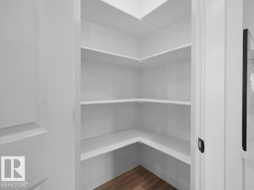 Walk-in pantry featuring multiple white shelves, wood-finish flooring, and a white paneled door - 18723 130 Street, Edmonton, AB 