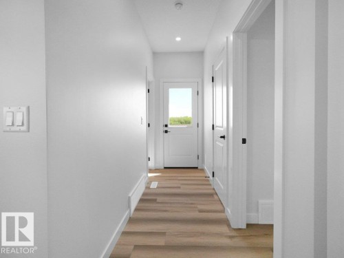 Hallway featuring wood-finish flooring, recessed lighting, white trim, white walls, and a white paneled door with dark hardware - 18723 130 Street, Edmonton, AB 