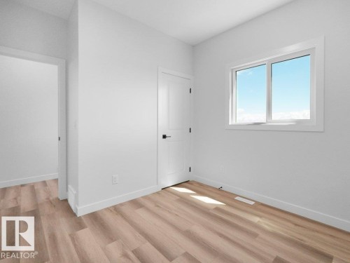 Bright interior space featuring a window with white trim, wood-finish flooring, white walls, and a white interior door with black hardware - 18723 130 Street, Edmonton, AB 