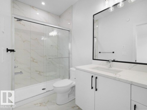 Modern bathroom featuring a glass-enclosed shower with white and gold-veined tile surround, a single-sink vanity with white cabinetry and black hardware, a coordinating black-framed mirror, and recessed lighting - 18723 130 Street, Edmonton, AB 