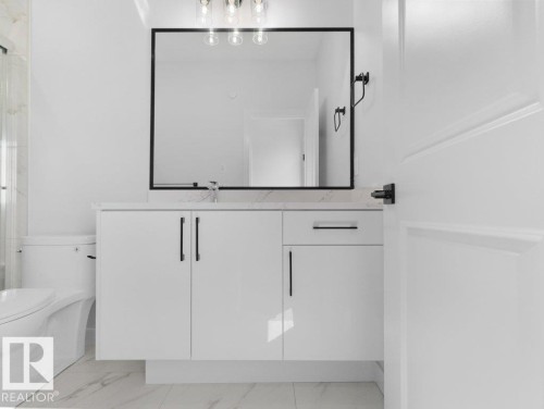 Contemporary bathroom featuring a white vanity with matte black hardware, a rectangular framed mirror, and a wall-mounted light fixture - 18723 130 Street, Edmonton, AB 