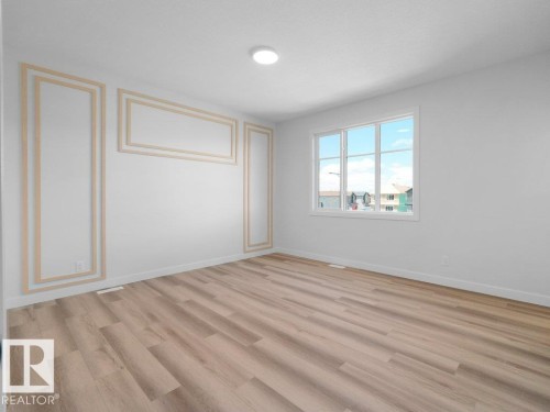 Spacious room featuring wood-finish flooring, crisp white walls, and decorative wall molding - 18723 130 Street, Edmonton, AB 