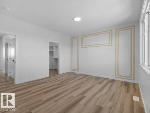 Spacious room featuring light wood-finish flooring, white walls with decorative panel molding, a recessed ceiling light, and a window providing natural illumination - 18723 130 Street, Edmonton, AB 