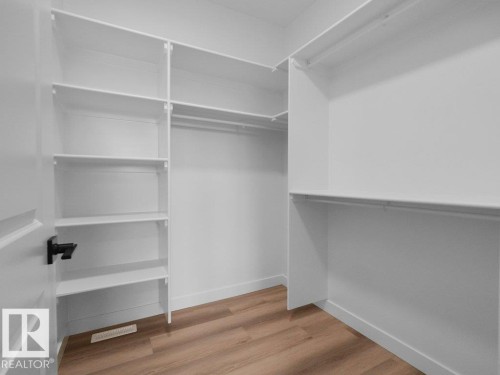 Walk-in closet featuring built-in shelving, multiple hanging rods, white trim, and wood-finish flooring - 18723 130 Street, Edmonton, AB 