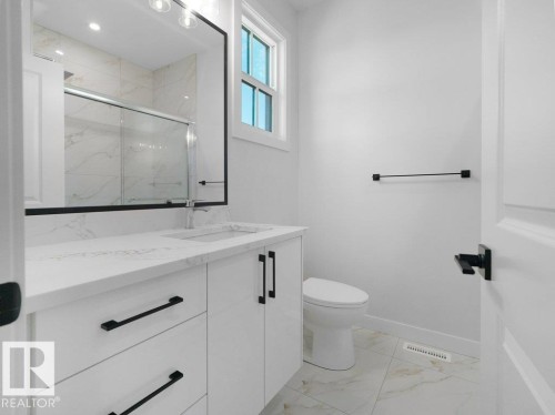 Bathroom featuring a white vanity with quartz-finish countertop, integrated sink, and black hardware - 18723 130 Street, Edmonton, AB 