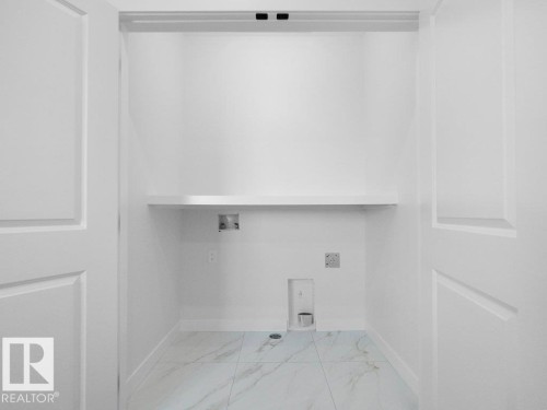 Dedicated laundry area featuring white panel doors, a built-in shelf, and light-toned tile flooring - 18723 130 Street, Edmonton, AB 