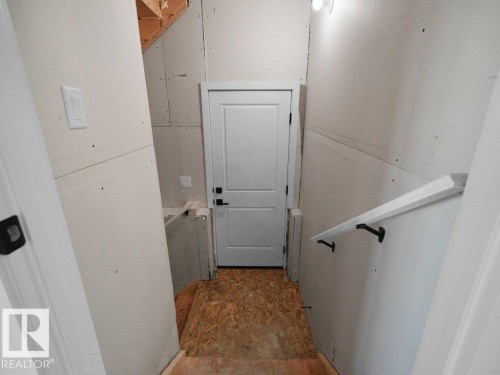 Unfinished basement space featuring a white paneled door, exposed wood framing, and an installed wall-mounted handrail - 18723 130 Street, Edmonton, AB 