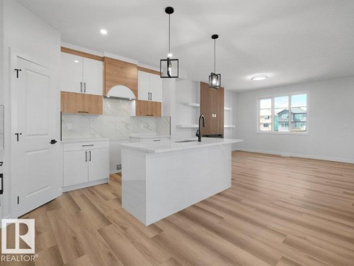 Modern kitchen featuring an island with a built-in sink, white cabinetry with wood-finish accents, a marble-look backsplash, and wood-finish flooring - 18723 130 Street, Edmonton, AB 