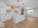Modern kitchen featuring an island with a built-in sink, white cabinetry with wood-finish accents, a marble-look backsplash, and wood-finish flooring - 18723 130 Street, Edmonton, AB 