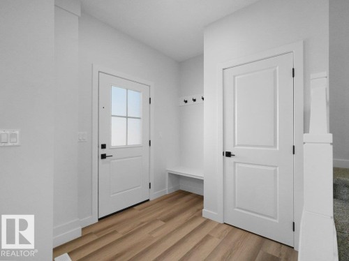 Entryway featuring wood-finish flooring, a built-in bench with coat hooks, a white paneled door with frosted glass inserts, and a second white paneled door, all accented with matte black hardware - 18723 130 Street, Edmonton, AB 