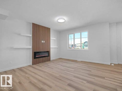 Spacious room featuring wood-finish flooring, a contemporary fireplace with slatted wood detailing, and white floating shelves - 18723 130 Street, Edmonton, AB 