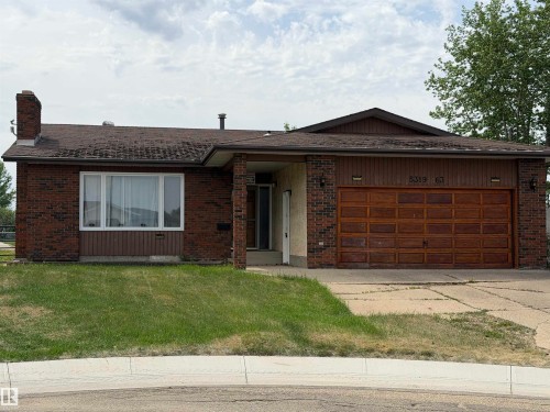 Brick facade residence featuring a two-car garage with a paneled wood-finish door, an asphalt shingle roof, a prominent front window, and a concrete driveway - 5319 63 Street, Redwater, AB 