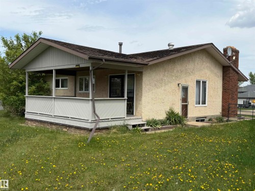Ranch-style residence featuring a covered front porch with white railing, stucco exterior, and a brick chimney - 5319 63 Street, Redwater, AB 