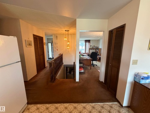 Interior hallway featuring wood railing, louvered bi-fold doors, and a decorative pendant light fixture - 5319 63 Street, Redwater, AB 