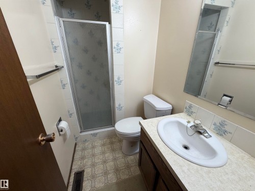 Bathroom featuring a single vanity with an integrated sink, a commode, and a shower enclosure - 5319 63 Street, Redwater, AB 