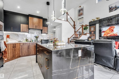 Contemporary kitchen featuring a large waterfall island with dark veined stone, two-tone cabinetry, marble-patterned backsplash, recessed lighting, and modern pendant fixtures - 208 33 Street, Edmonton, AB 