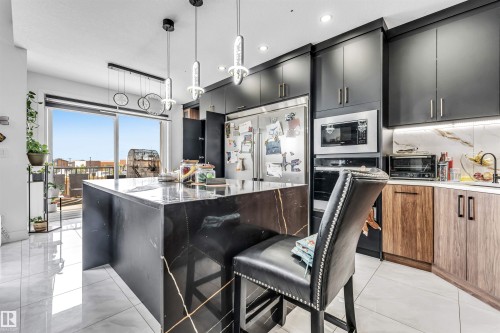 Kitchen featuring a waterfall island with a dark stone surface, pendant lighting, stainless steel appliances, dark cabinetry, and light tile flooring - 208 33 Street, Edmonton, AB 