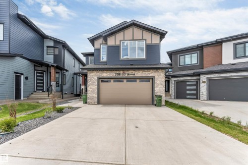 Modern two-story residence featuring a stone-clad garage, contemporary blue siding, contrasting beige accents, a paved driveway, and large windows - 208 33 Street, Edmonton, AB 