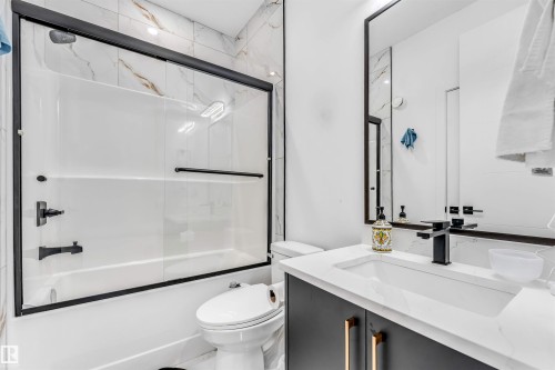 Contemporary bathroom featuring a white bathtub with sliding glass doors, matte black fixtures, and marble-patterned wall tiling - 208 33 Street, Edmonton, AB 