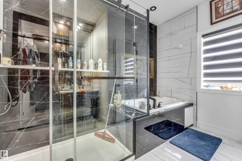 Contemporary bathroom featuring a walk-in shower with clear glass enclosure, black marbled wall tiling, a built-in soaking tub, and contrasting white wall tiling - 208 33 Street, Edmonton, AB 