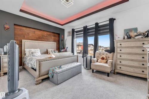 Recessed tray ceiling with accent lighting, wood-paneled feature wall, large windows with roller shades, and light-toned carpet - 208 33 Street, Edmonton, AB 
